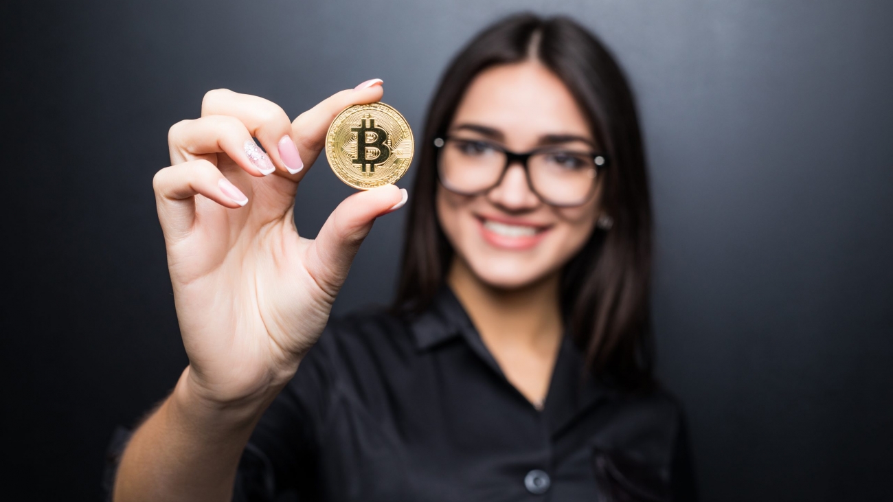 young successful confident woman with glasses holds a gold bitcoin in her hand