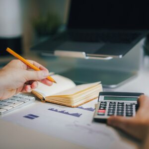 Pessoa analisando documentos financeiros com calculadora e anotações em mesa de trabalho