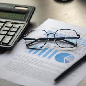 Documentos financeiros com calculadora, caneta e óculos sobre mesa de trabalho