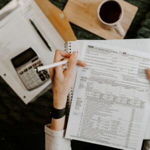Pessoa revisando documentos financeiros com calculadora e laptop sobre a mesa