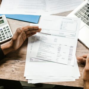 Pessoas revisando documentos financeiros sobre a mesa com calculadora e notebook