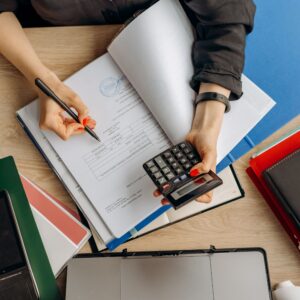 Pessoa analisando documentos fiscais e financeiros com calculadora em mesa de escritório