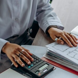 Pessoa calculando valores em documentos financeiros com calculadora sobre mesa de escritório