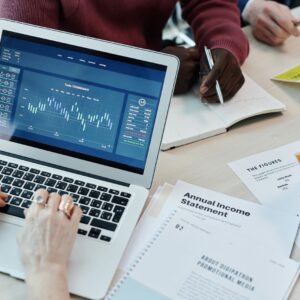 Profissionais analisando dados financeiros em laptop durante reunião, com gráficos e relatórios na tela