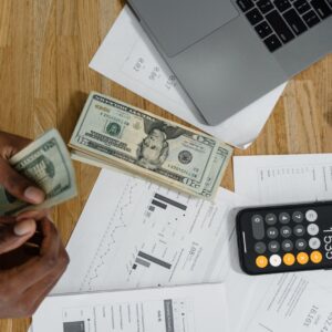 Maos contando cedulas com calculadora, graficos financeiros e laptop na mesa de trabalho