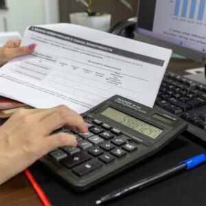 Pessoa calculando dados financeiros com calculadora e documento em uma mesa de trabalho